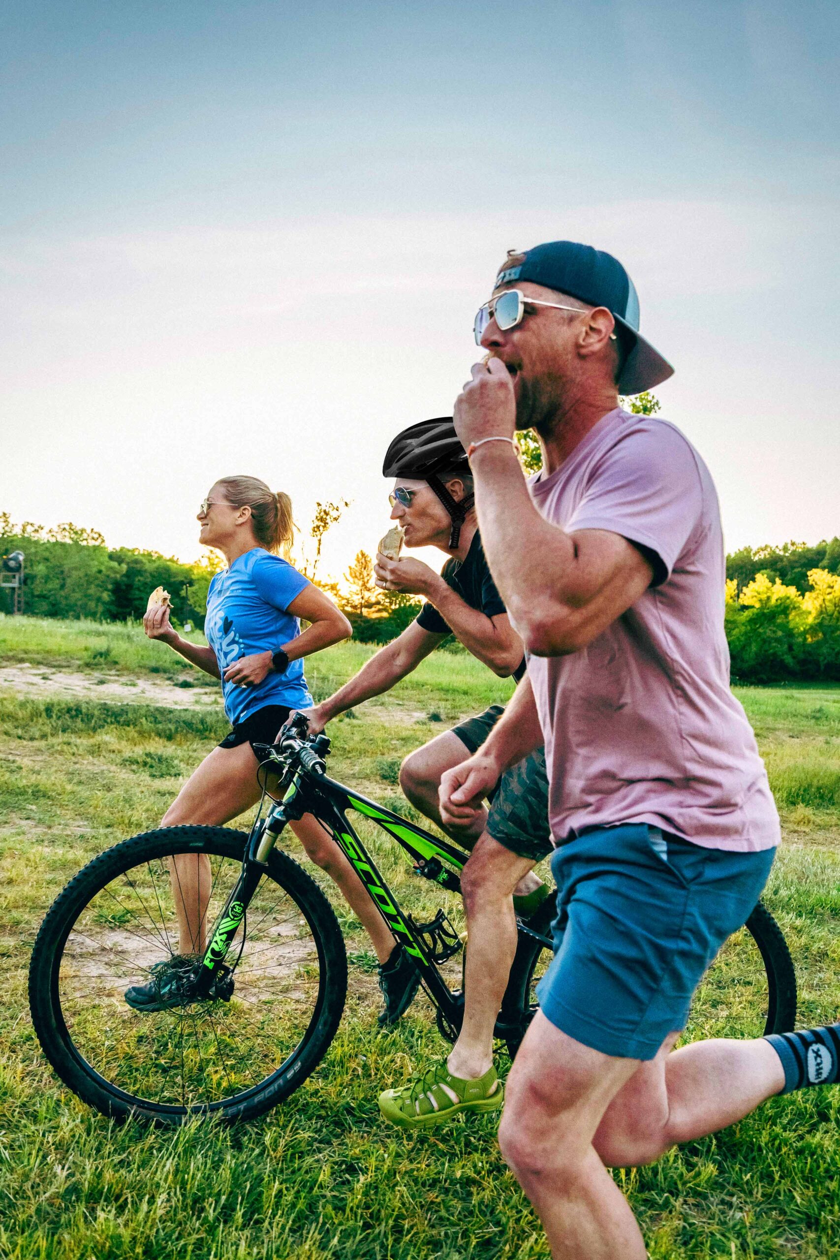 Two runners and a mountain biker eating a taco while running and biking next to eachother.